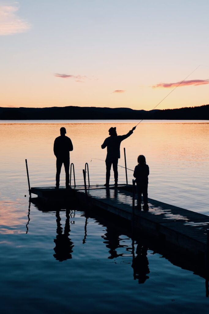 pexels-photo-988622-988622 A serene scene of a family fishing together on a lake dock at sunset, creating silhouettes on the water.